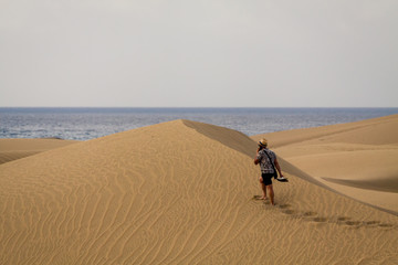 Man is walking alone by sand dunes and is calling by mobile phone.