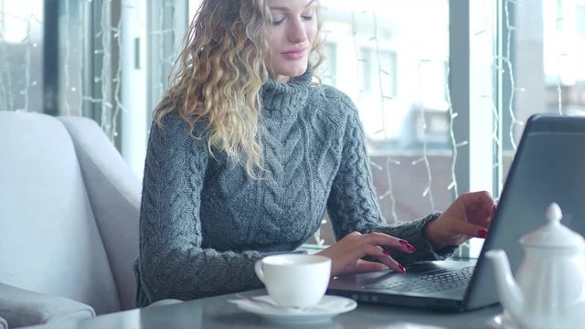 Businesswoman typing text on a laptop sitting in a cafe over a Cup of tea.