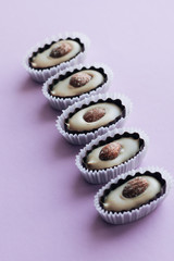 Row of delicious praline sweets with almonds on purple background