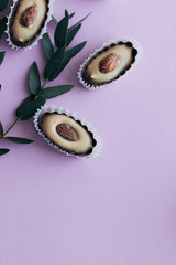 Composition of delicious praline sweets with almonds and green twigs on purple background