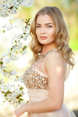 Fototapeta premium Spring. Vertical portrait of a beautiful girl near blooming tree