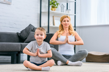Mother with little son practicing yoga in lotus position in living room