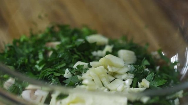 Close up of unrecognizable cook pouring water on freshly chopped garlic cloves and green parsley, then sprinkling salt and pepper