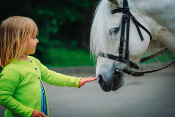 little girl touching big horse in nature