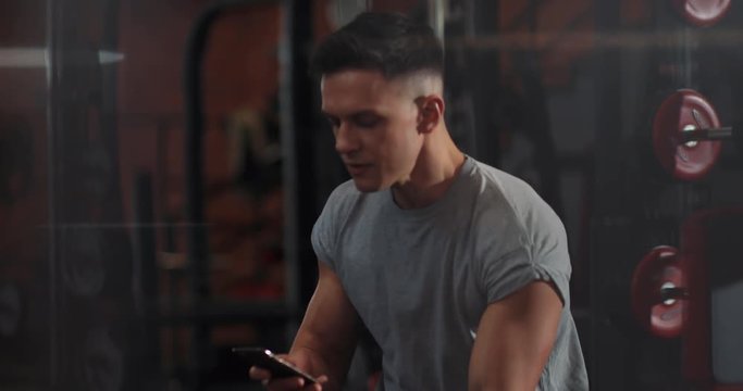Handsome young man use phone drink water in gym sportsman sport fitness internet face technology fit lifestyle male workout athlete sportswear networking body exercise healthy mobile smartphone