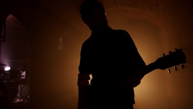 A silhouette of a man playing guitar at dark brick room.