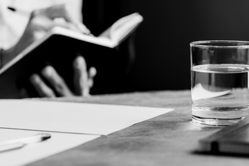 The man is writing in a notebook in a workplace. The concept of a work and education. Black and white photography.