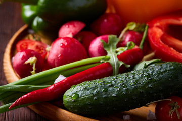 Wooden plate with vegetables for a vegetarian salad on rustic wooden background, close-up, selective focus