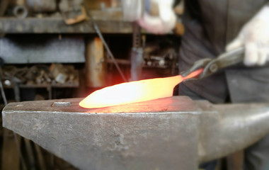 Making the knife out of metal at the forge. Close up blacksmith's hands taking a hammer and hitting hot metal on an anvil. - Powered by Adobe