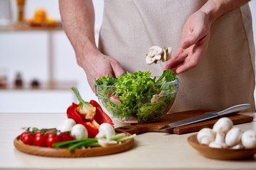 Man cooking at kitchen making healthy vegetable salad, close-up, selective focus.