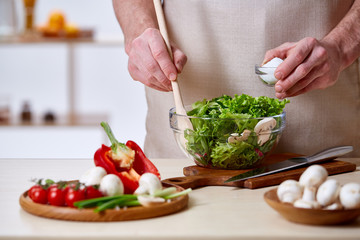 Man cooking at kitchen making healthy vegetable salad, close-up, selective focus.