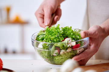 Man cooking at kitchen making healthy vegetable salad, close-up, selective focus.
