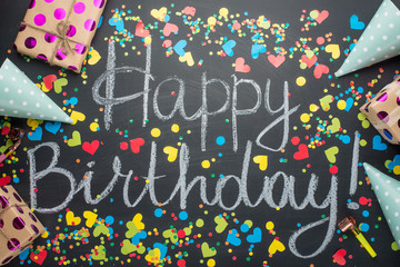 Happy birthday sign on the board with gifts and confetti. View from above