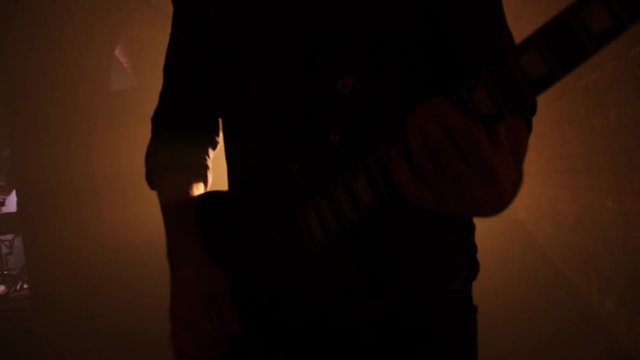 A silhouette of a man playing guitar at dark brick room.