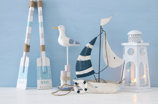 nautical concept with white decorative seagull bird, lighthous lantern, wooden oars and boat over blue background.