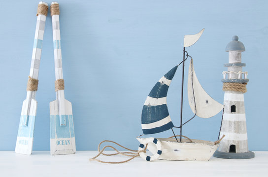 nautical concept image with decorative oars, boat and lighthouse over light blue background.