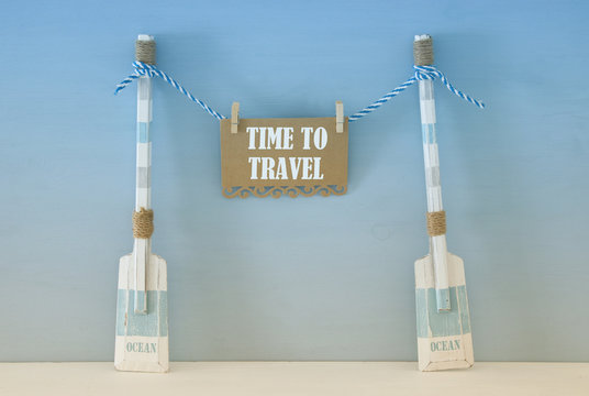 nautical concept with wooden decorative boat oars and note hanging on a string over blue background.
