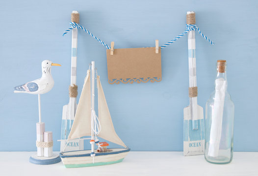 nautical concept with hanging empty note on a string next to boat, letter in the bottle and seagull over blue background.