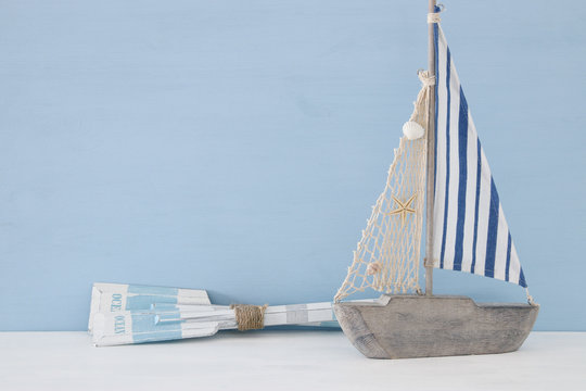 nautical concept with sail boat and wooden oars over blue background.