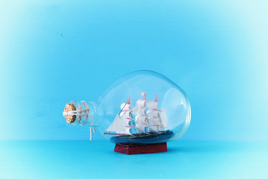 nautical concept image with sail boat in the bottle over blue wooden table and background. Selective focus.