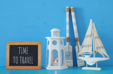 nautical concept with white decorative lighthouse lantern, wooden oars and boat next to blackboard over blue background.