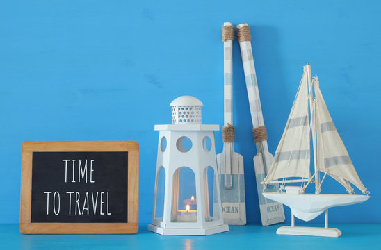 nautical concept with white decorative lighthouse lantern, wooden oars and boat next to blackboard over blue background.