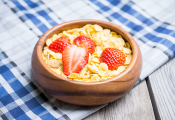 Corn flakes with strawberry in wooden bowl. Selective focus.