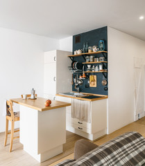 Design of modern home kitchen in the attic and rustic style. Black wall with shelves, trays, jars, mugs. Refrigerator, dining table, chairs and sofa in the foreground. Residential Loft studio.