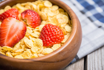 Corn flakes with strawberry in wooden bowl. Selective focus.