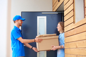 Smiling delivery man in blue uniform delivering parcel box to recipient - courier service concept. Smiling delivery man in blue uniform