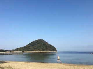 Fototapeta premium Man running on sandy beach with blue sky background