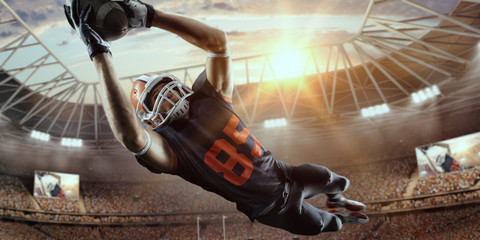 American football player jumps and catches the ball in flight in professional sport stadium - obrazy, fototapety, plakaty