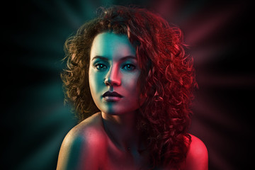 Portrait of cute red head girl with curly hair in colorful bright lights posing in studio