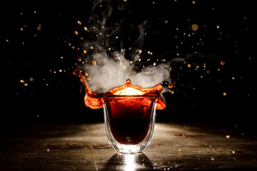 Splash of the coffee from the transparent glass on the dark background