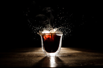 Splash of the hot coffee from the transparent glass on the dark background