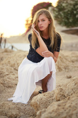Fototapeta na wymiar Blonde caucasian woman wearing dark blue lace top and white skirt. Posing on rock by the sea in Egypt.