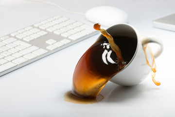 Falling and spilling of a cup of coffee on top of a desk with a computer