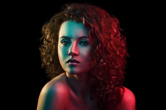 Portrait of cute red head girl with curly hair in colorful bright lights posing in studio