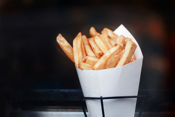 French fries in paper bundle. Street food. Dark background. Place for text and copyspace....