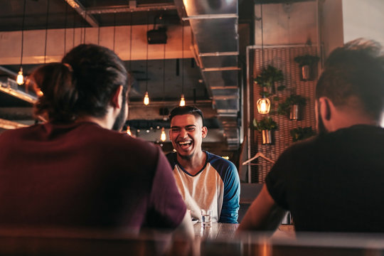 Group of mixed race young men talking and laughing in lounge bar. Multiracial friends having fun in cafe