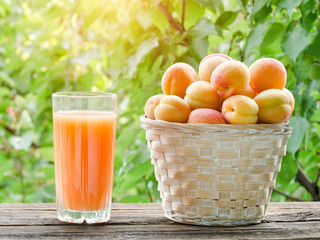 Apricots in a wicker basket and a glass of juice on a green background, sunlight
