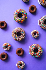 Baked chocolate doughnuts with glaze and confectionary topping on a violet background. Top view.