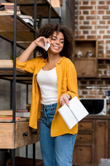 beautiful young woman with book talking by phone at home