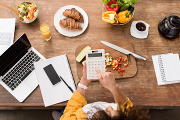 top view of young woman working with digital devices at kitchen during breakfast