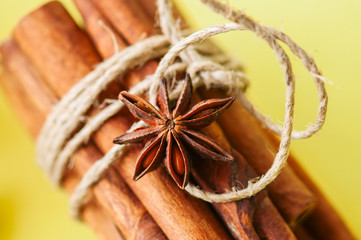 Close up of tied cinnamon sticks and anise star, Yellow background.