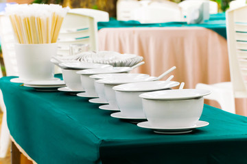 Stacked white clean plates and bowls on a light table are placed for served.