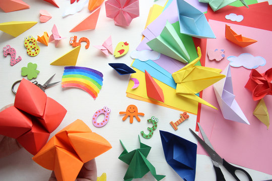 Man doing origami. Multicolored Origami and paper on  a white table.