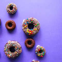 Baked chocolate doughnuts with glaze and confectionary topping on a violet background. Top view. Square image.