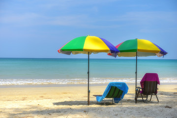 Beach chair under colourful umbrella on tropical beach background, summer time concept