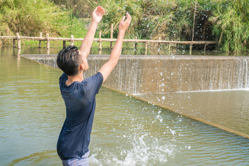 Relaxing for life, natural therapy concept : Asian Young man playing fun making splash with drops in water river in hot summer day at outdoors